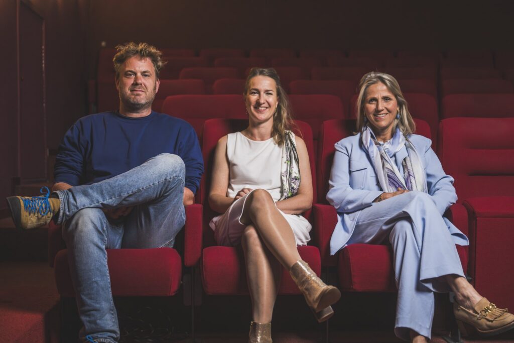 Drie toeschouwers in een bioscoopzaal met rode zetels
