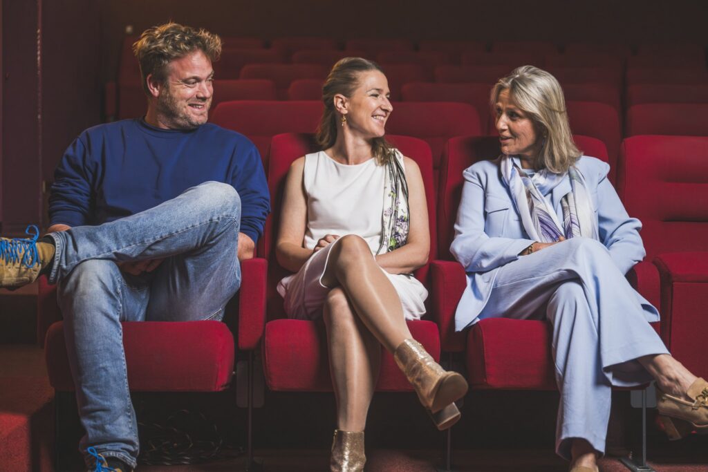 Drie toeschouwers in een bioscoopzaal met rode zetels